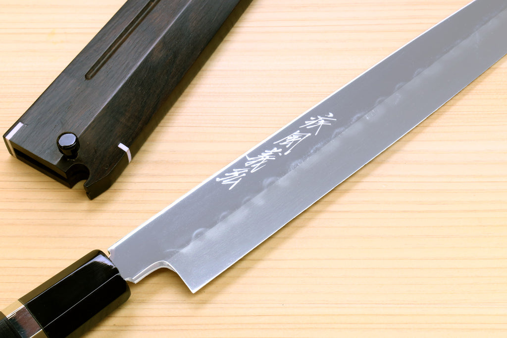 Long mirror-finished steel knife blade with etched text and black handle, side angle.