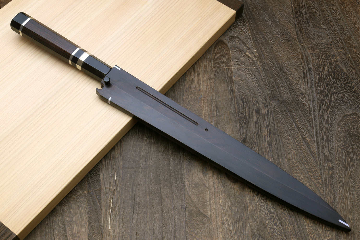 Long mirror-finished steel knife with dark handle and etched details, profile view.