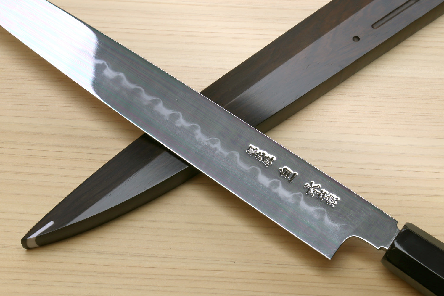 Mirror-finished steel knife blade with etched details and dark handle, diagonal view.