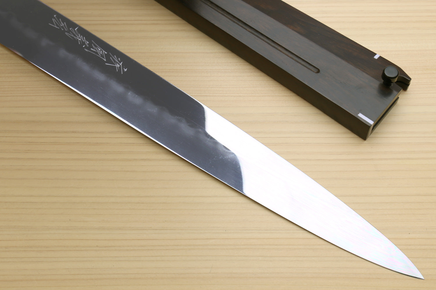 Mirror-finished steel knife blade with etched text, pointed tip and dark handle.