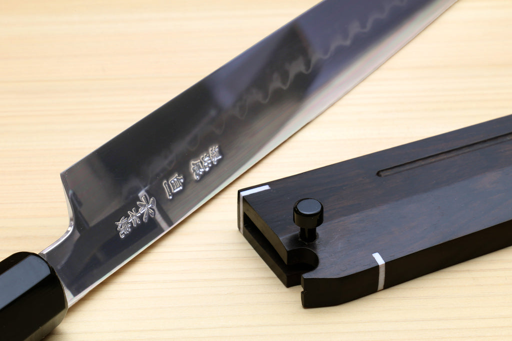 Mirror-finished steel blade with etched markings and dark handle; maker stamp visible.