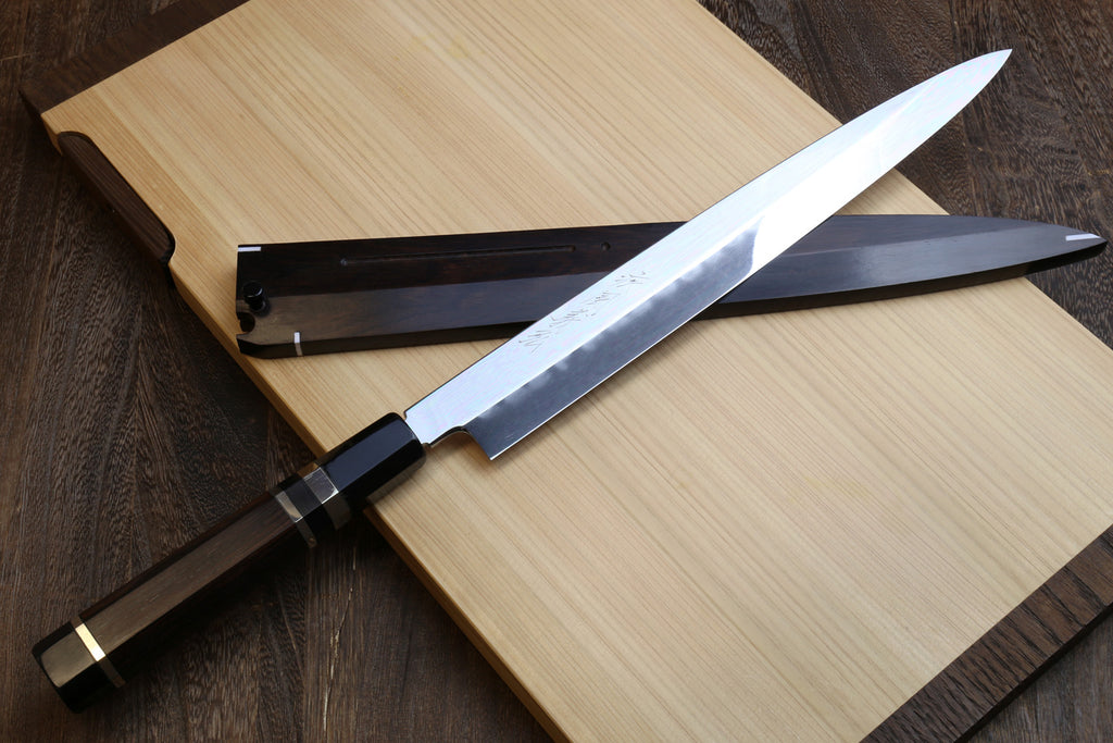 Mirror-finished steel knife and dark handle resting near blade sheath, angled view.