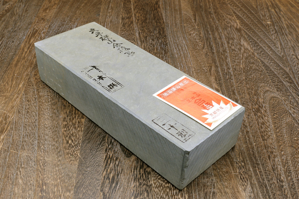 Natural whetstone finishing stone block, light gray with orange label stickers on top.