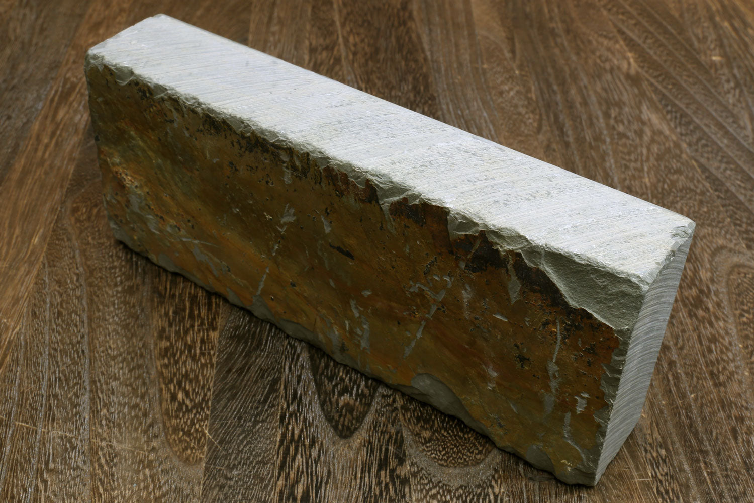 Natural sharpening whetstone, rectangular honing stone with pale top and dark sides.