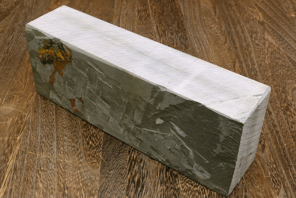 Natural sharpening whetstone, side view of long rectangular gray stone with stamped marks