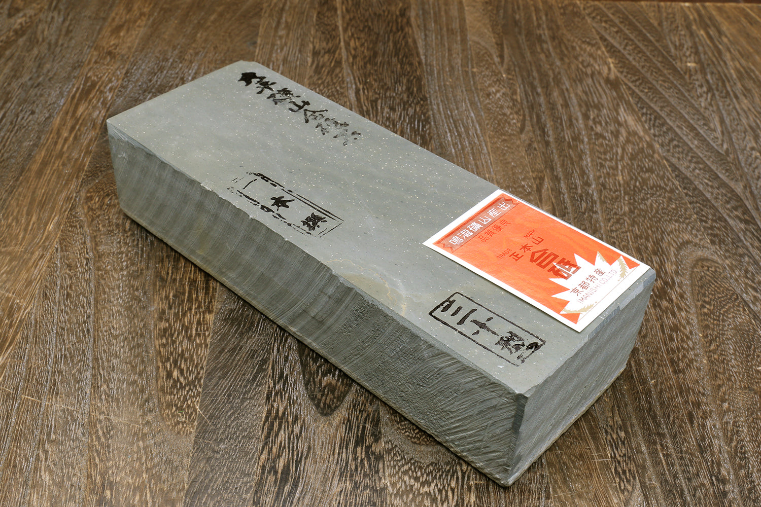 Natural whetstone finishing stone, grey rectangular bar with orange label and black text