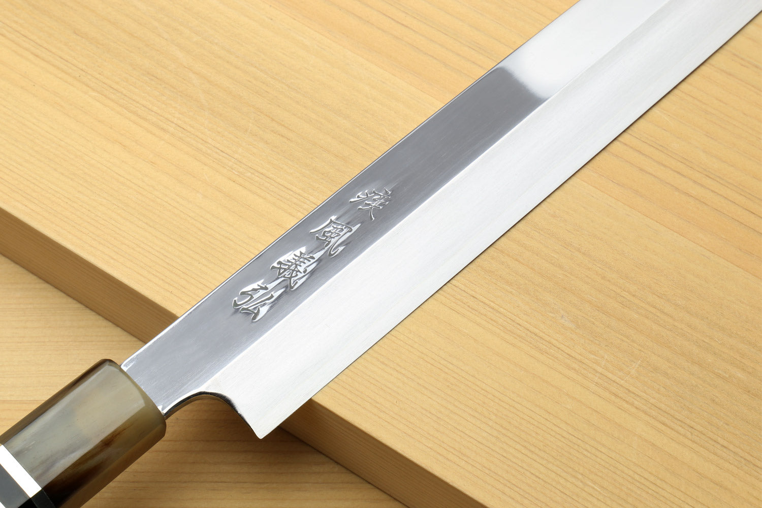Yanagi sushi knife close-up: mirror-finished blade with etched mark and horn bolster