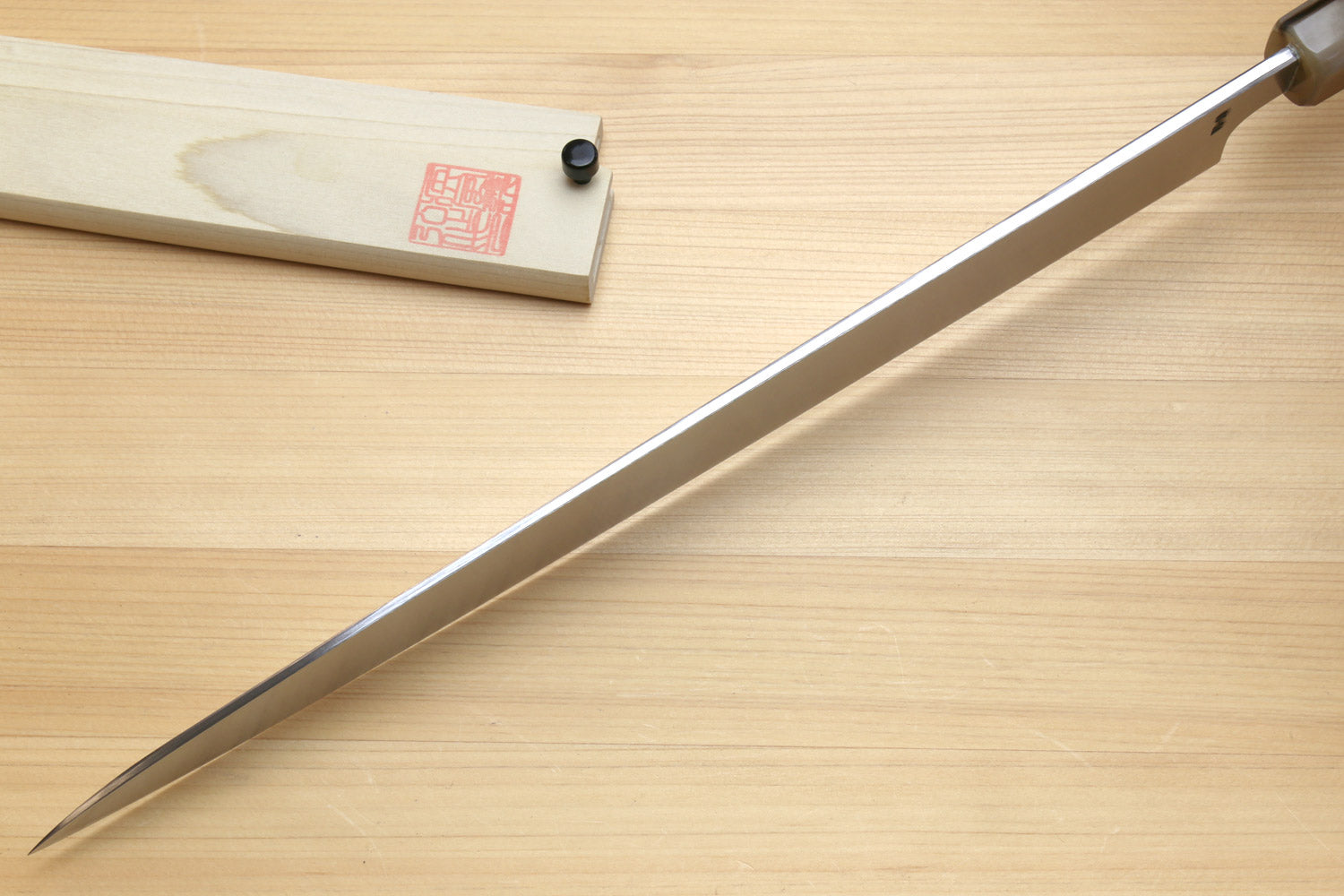 Yanagi sushi knife with mirror blade, horn handle, and wooden sheath on table