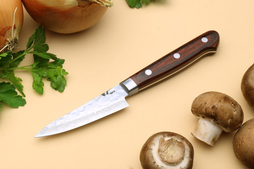 Paring knife on its side view, dark brown wood handle, hammered Damascus steel blade