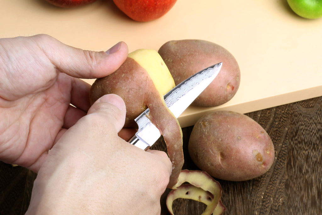 Paring knife with dark brown wood handle shown in hand, hammered Damascus blade