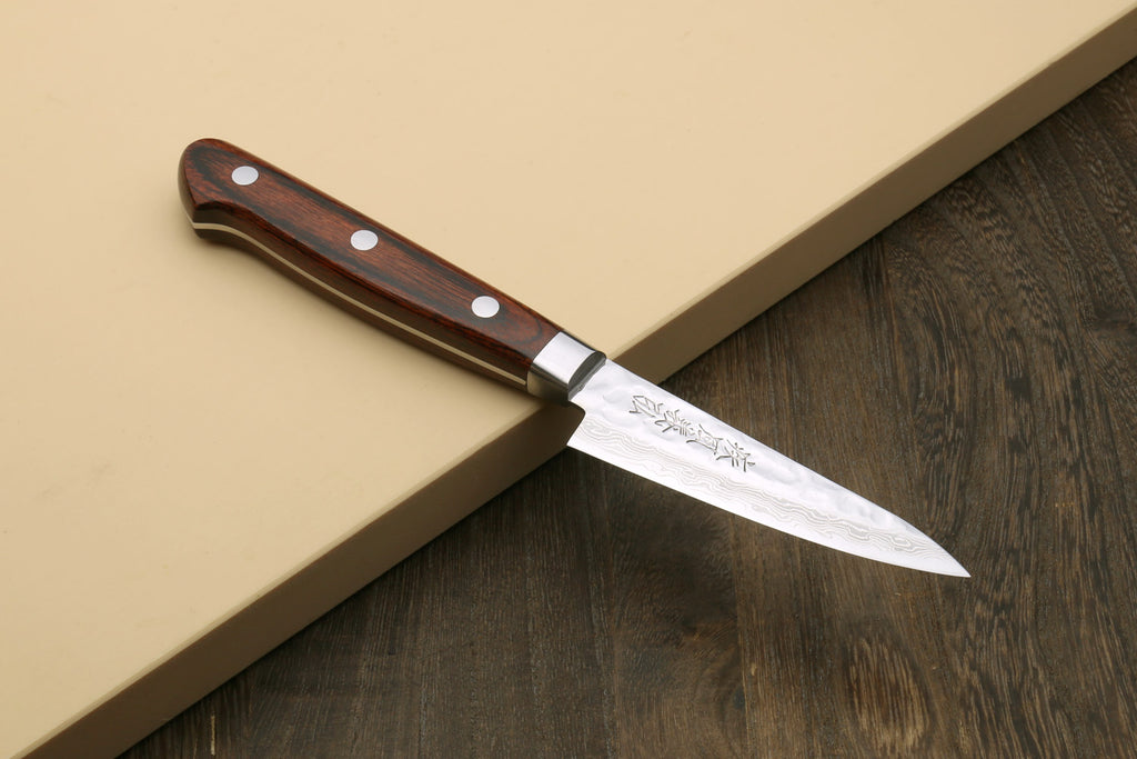 Paring knife placed at an angle, dark brown wood handle and Damascus stainless blade