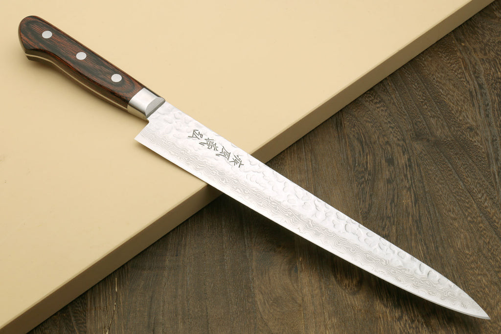 Sujihiki chef knife with hammered Damascus blade and dark wooden handle on board
