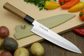 Damascus gyuto chef's knife with black bolster, light handle, and pointed blade