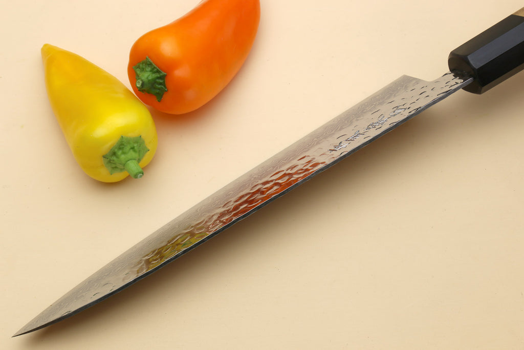 Damascus gyuto chef's knife with black bolster, light handle, and sharp tip