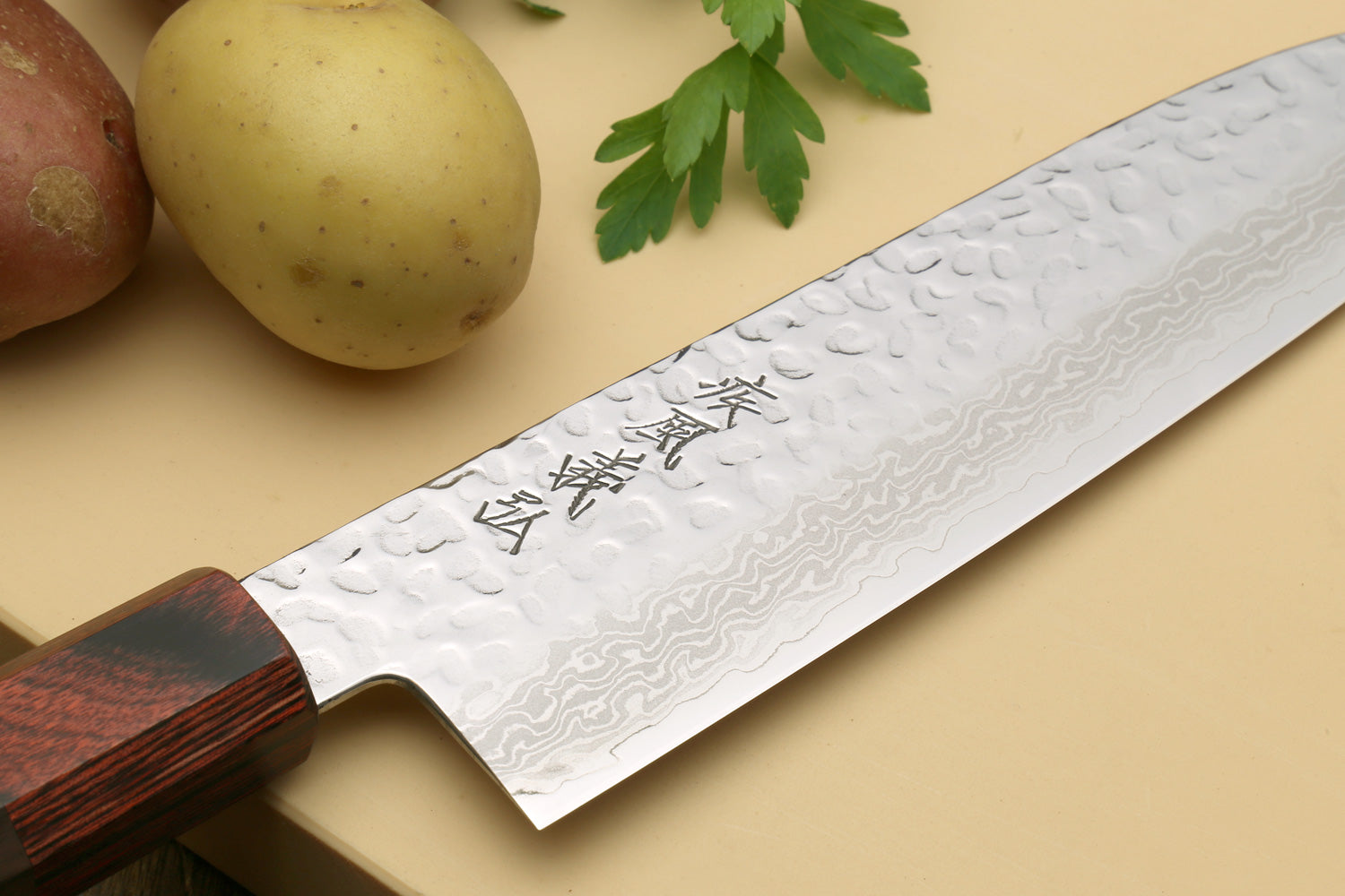 Damascus santoku knife blade close-up with carved kanji marks and dark octagonal handle.