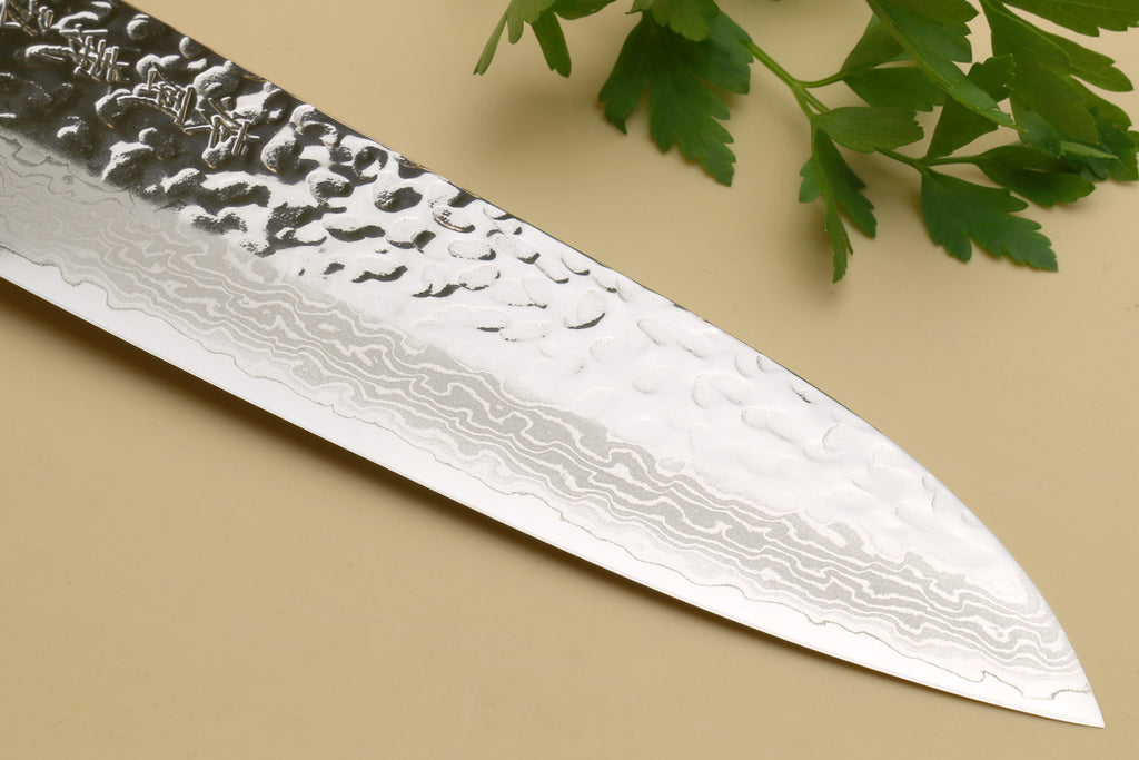 Damascus santoku knife blade close-up showing hammered wavy pattern and pointed tip.