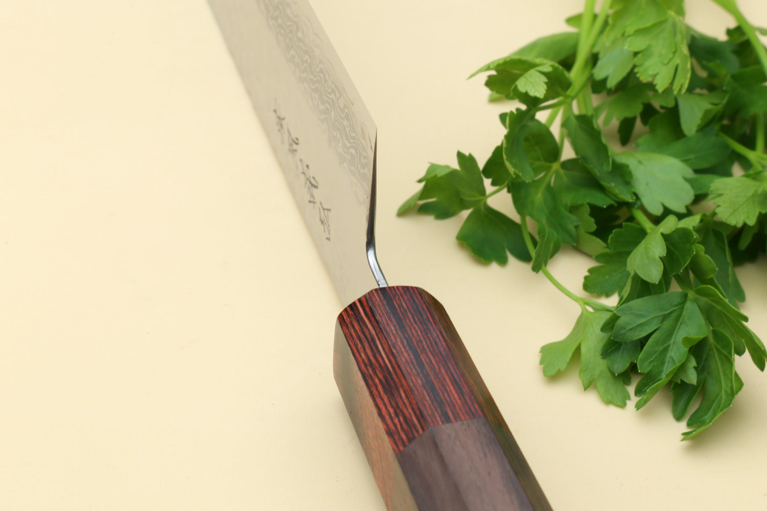 Santoku knife handle detail with dark rosewood scales and silver Damascus blade near herbs.