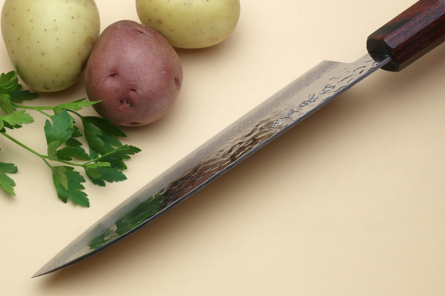 Damascus santoku knife, angled view, pointed tip and dark octagonal handle on board.