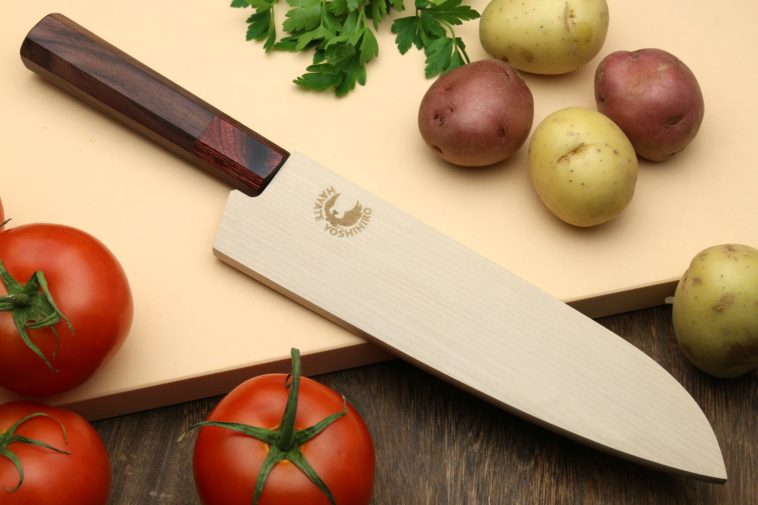 Santoku knife with dark octagonal rosewood handle and silver Damascus blade on board.