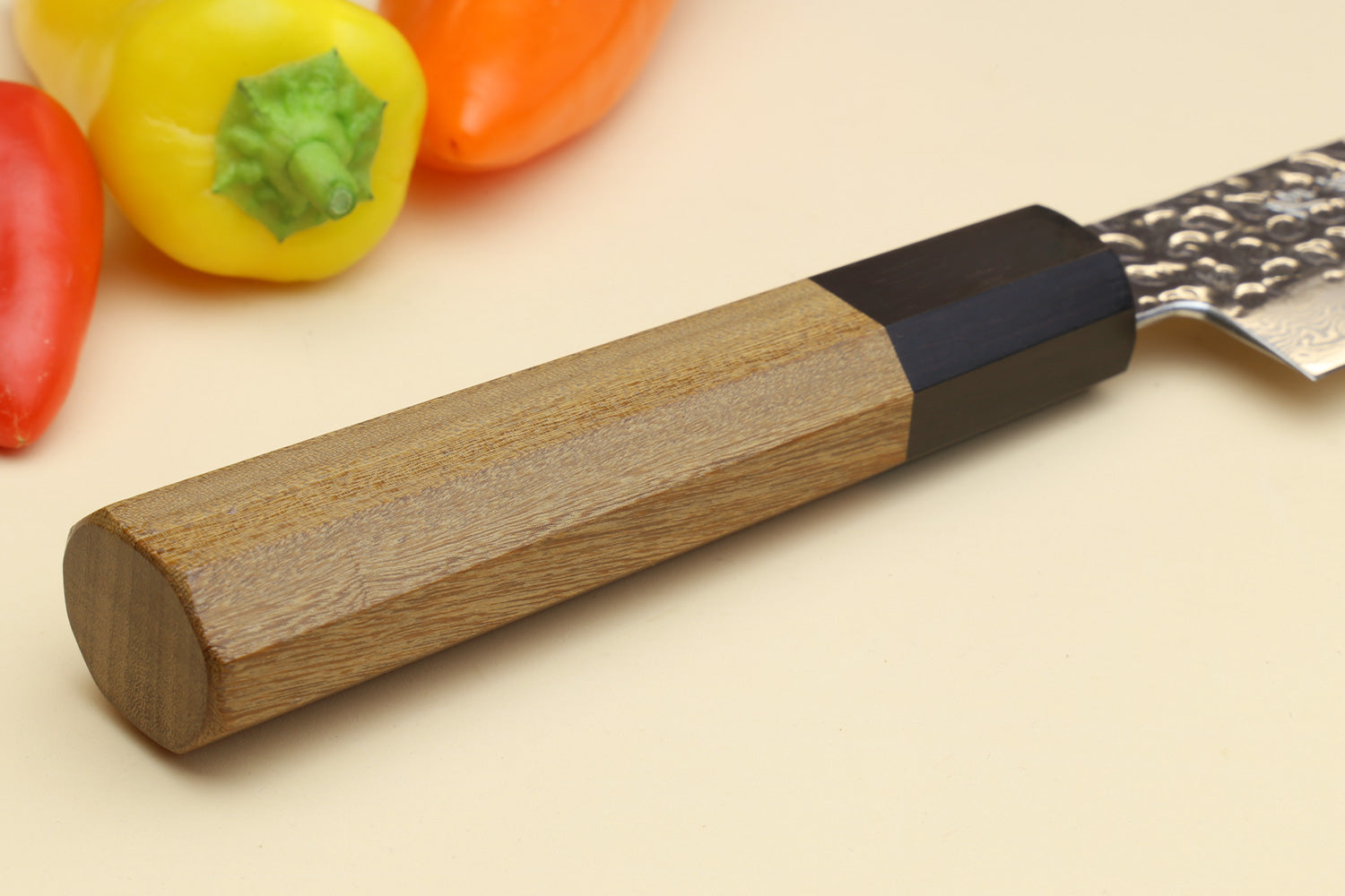 Octagonal wood handle with dark bolster on a Damascus sujihiki slicer knife