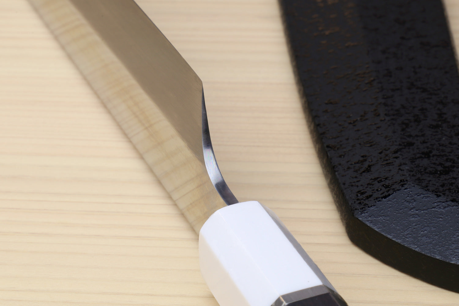 Japanese sushi sashimi knife with dark blade tip and ebony textured handle near bolster
