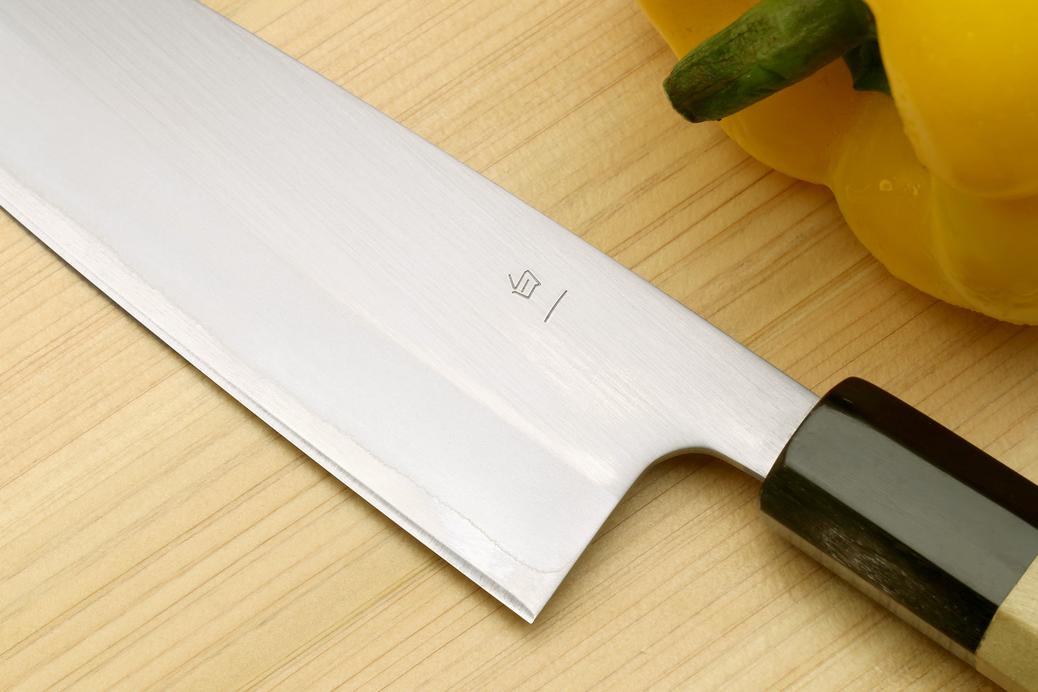 Stainless santoku knife with dark bolster and magnolia wood handle, blade close-up