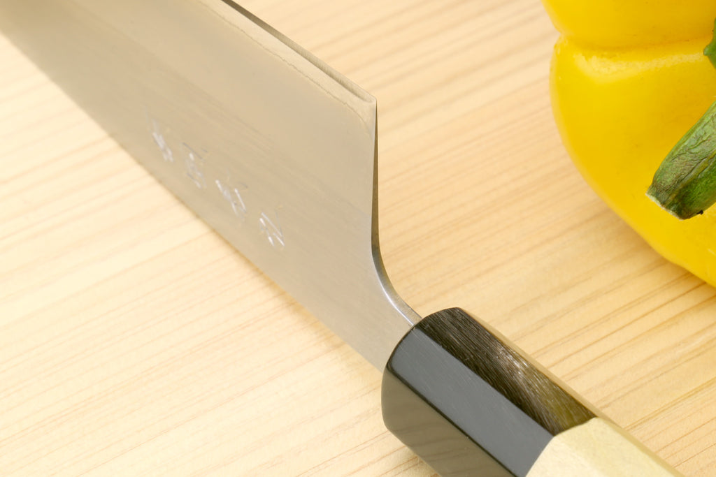Stainless santoku knife close-up of blade tang and dark bolster with magnolia wood