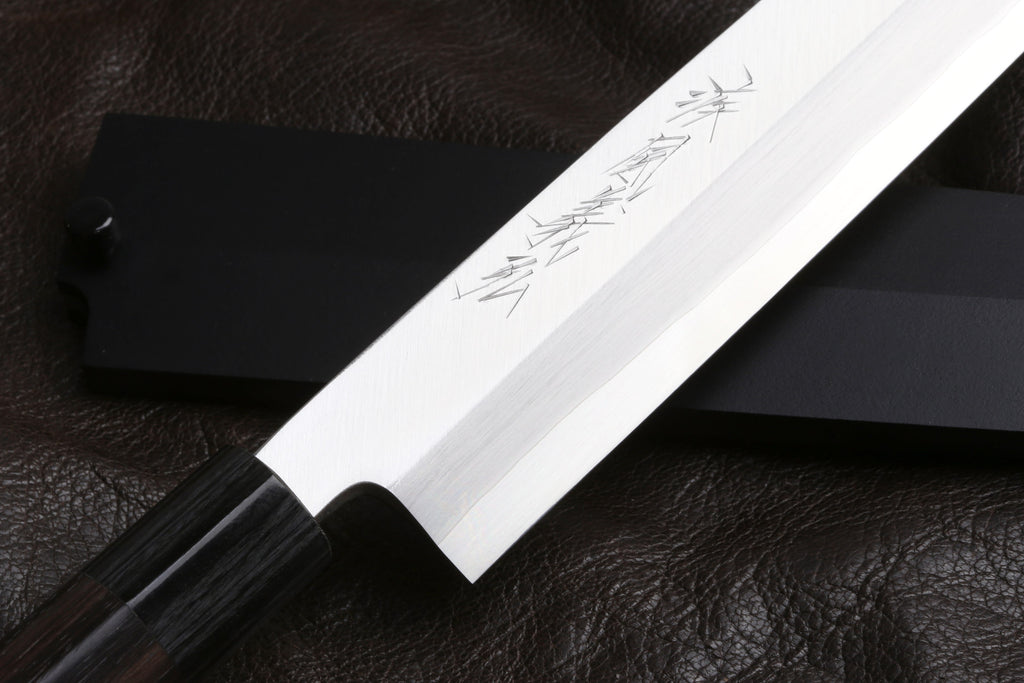 Stainless Yanagi knife blade close-up with etched markings and sharp tip