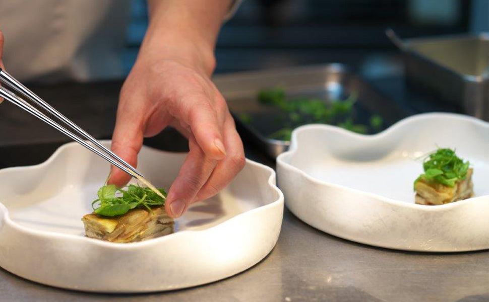 Plating tweezers with metal tips placing herbs on small white ceramic plates