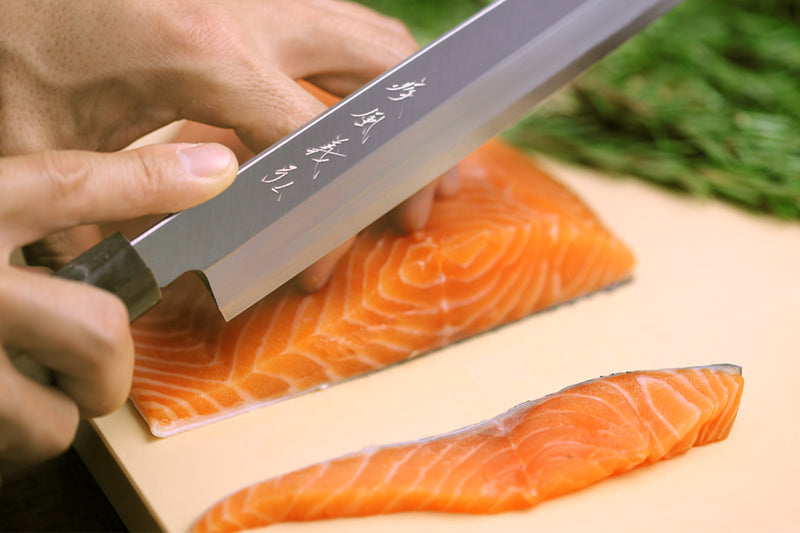 Japanese cutting board with salmon fillets and a chef slicing knife in hand.