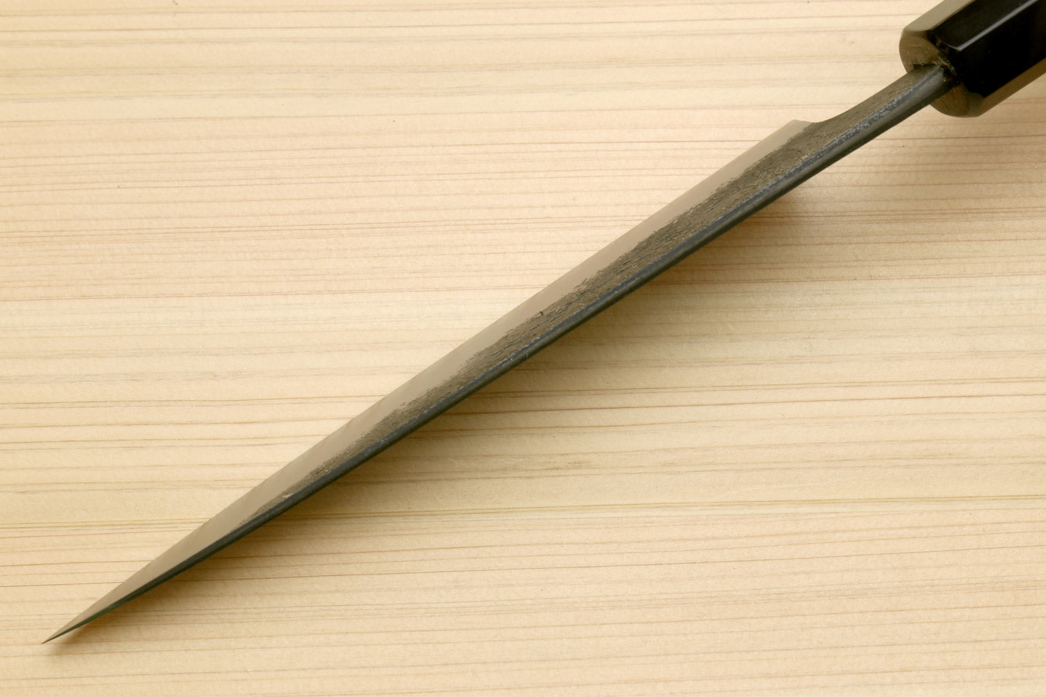 Japanese petty utility knife with pointed blade and dark bolster near handle