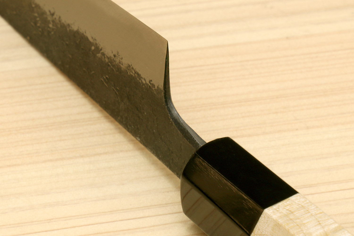 Petty utility knife blade junction with curved heel and black bolster on wood handle
