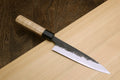 Petty utility knife with dark speckled blade and black bolster on light wood handle