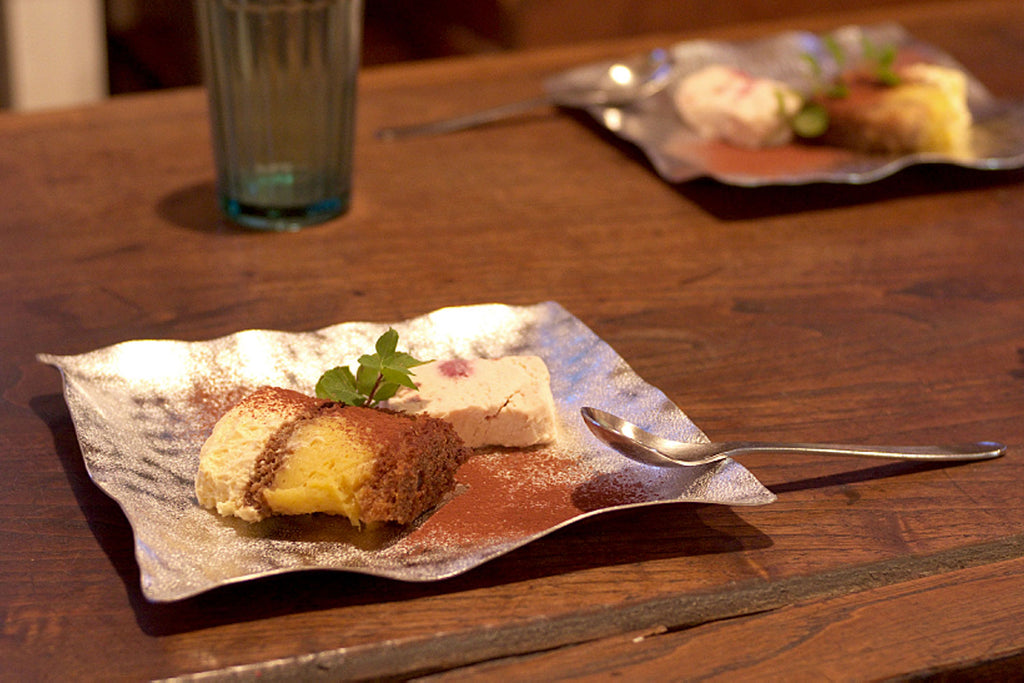 Flexible tin plate with dessert piece and small garnish, with spoon nearby