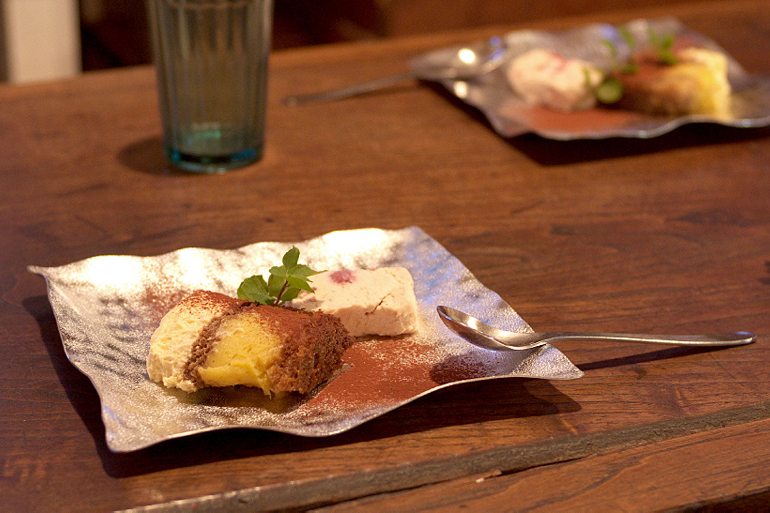 Flexible tin plate with dessert piece and small garnish, with spoon nearby