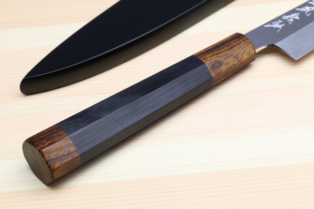 Petty utility knife with dark handle in dark saya cover, shown from side angle