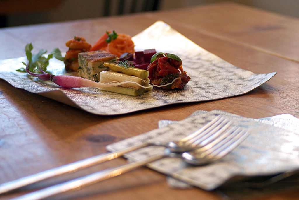 Flexible tin plate with raised edges, holding assorted appetizers on a table