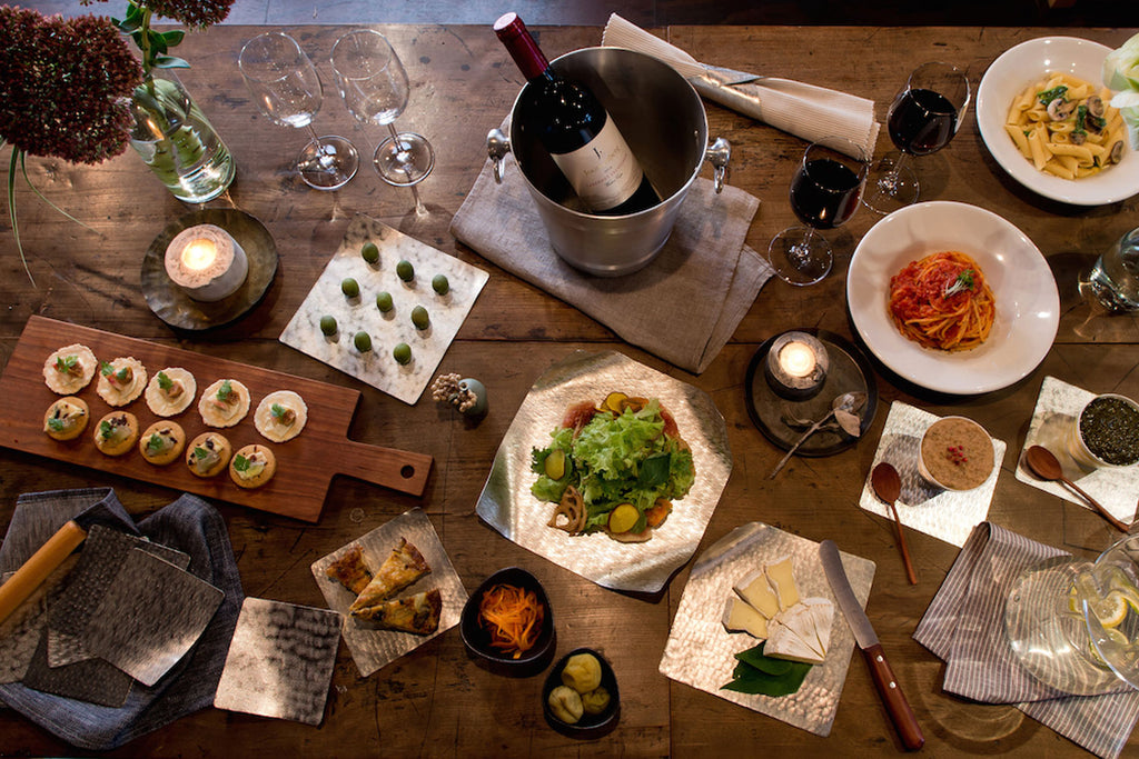 Multiple flexible tin plates with small dishes, drinks, and serving utensils