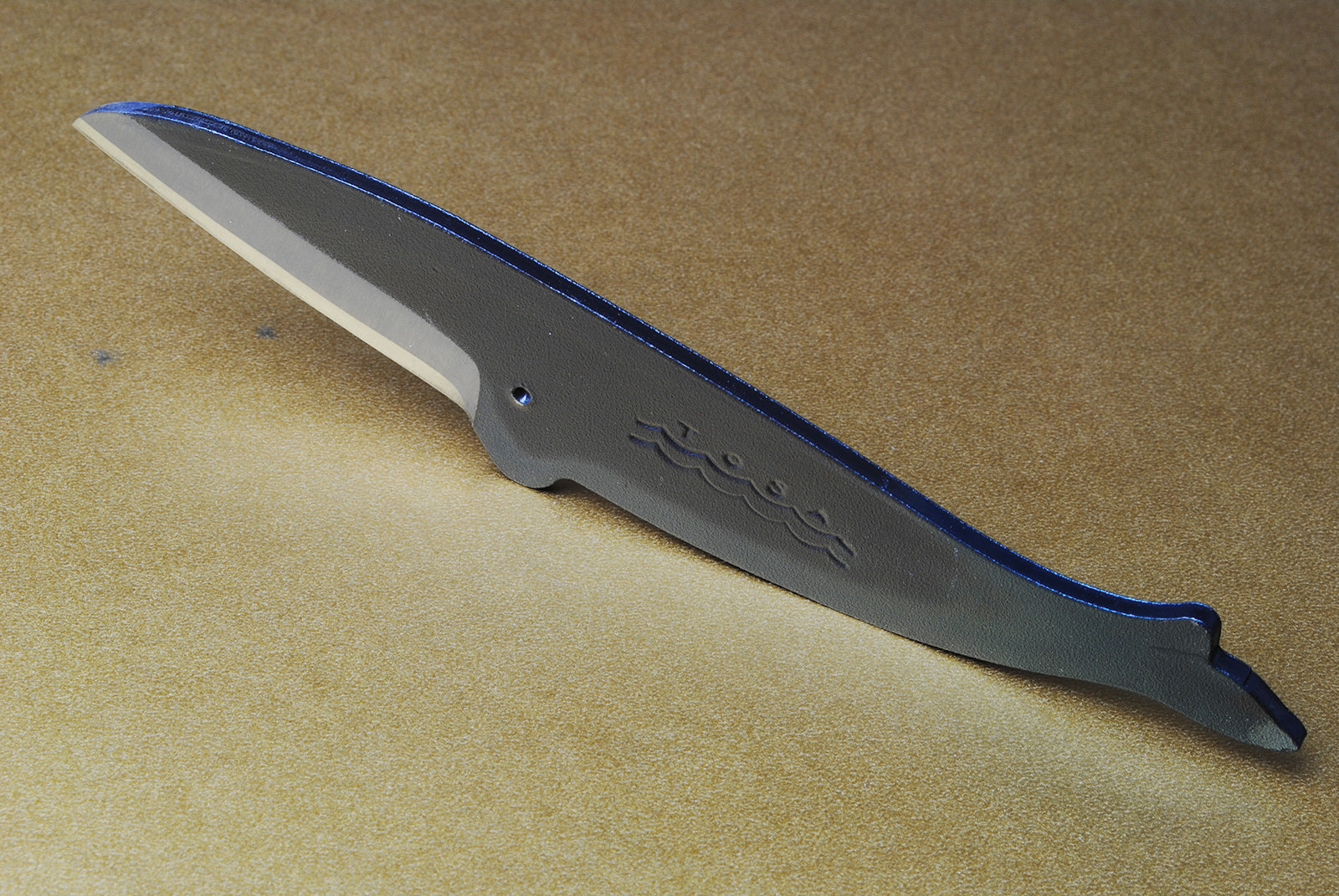 Japanese utility knife with dark blade, wave engraving, and reflective cutting edge