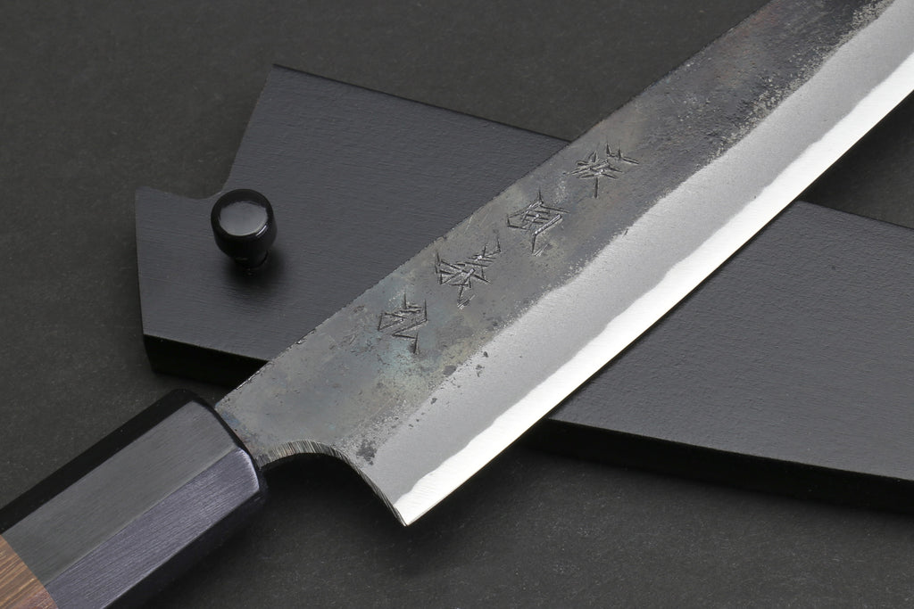Kurouchi-finished steel petty blade with engraved characters and dark handle end.