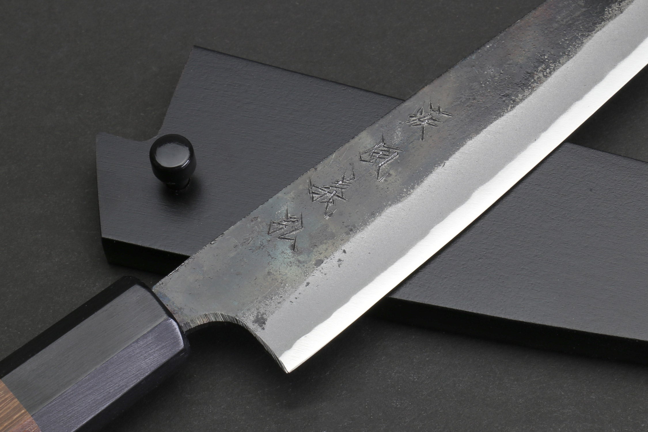 Kurouchi-finished steel petty blade with engraved characters and dark handle end.