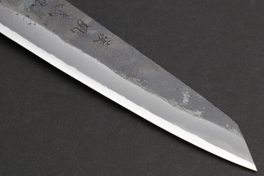 Petty utility knife tip with kurouchi-finished steel and small engraved mark.