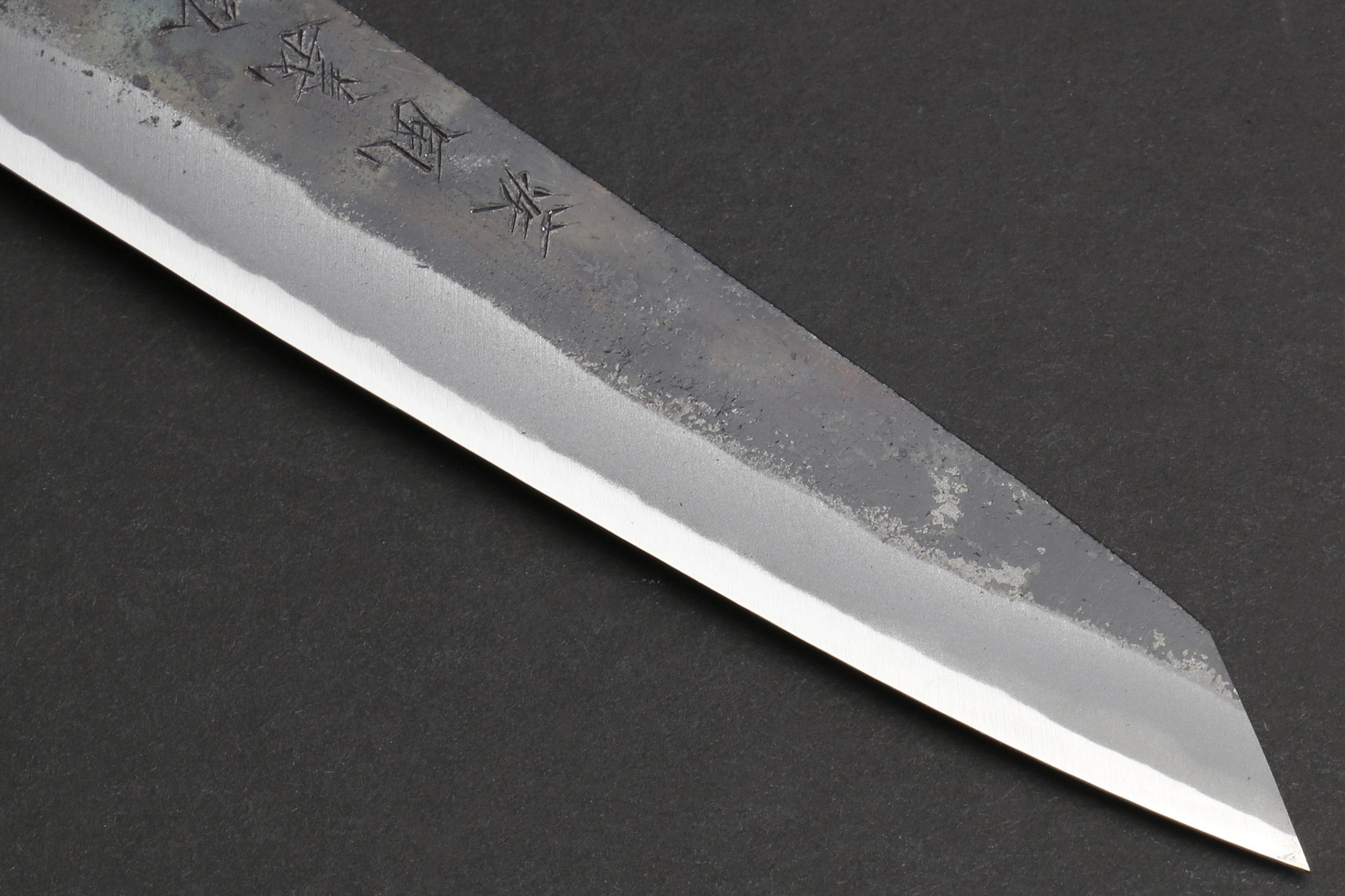 Petty utility knife tip with kurouchi-finished steel and small engraved mark.