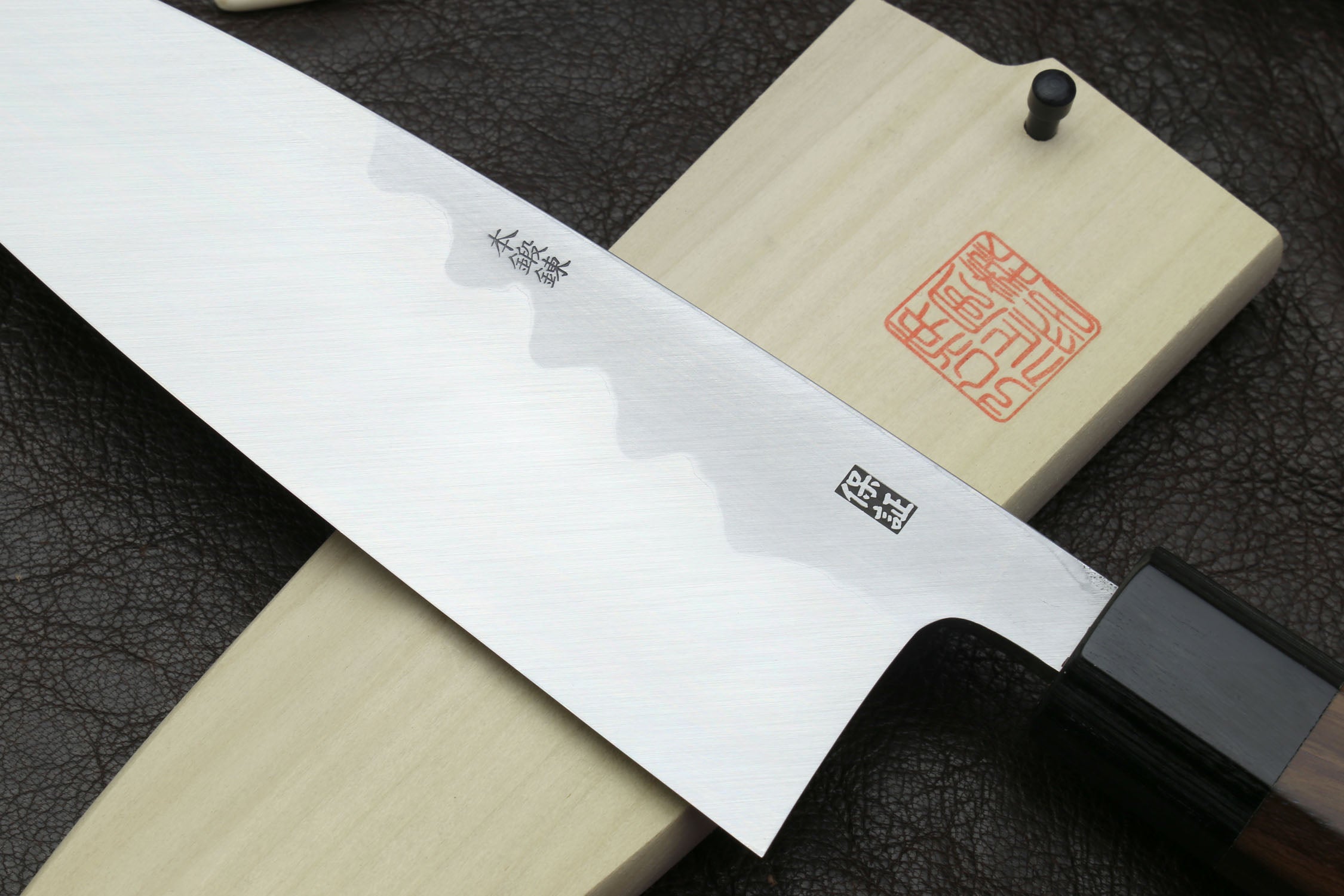 Japanese deba knife with white blade, dark handle, and light wooden saya