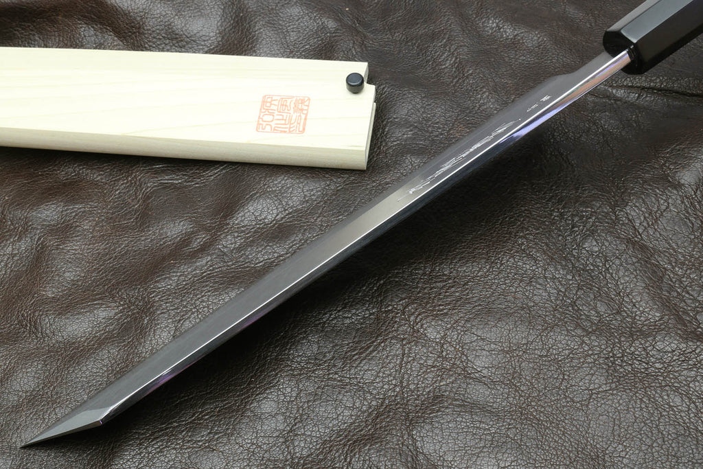 Multipurpose chef knife with silver blade and black handle beside light wood sheath