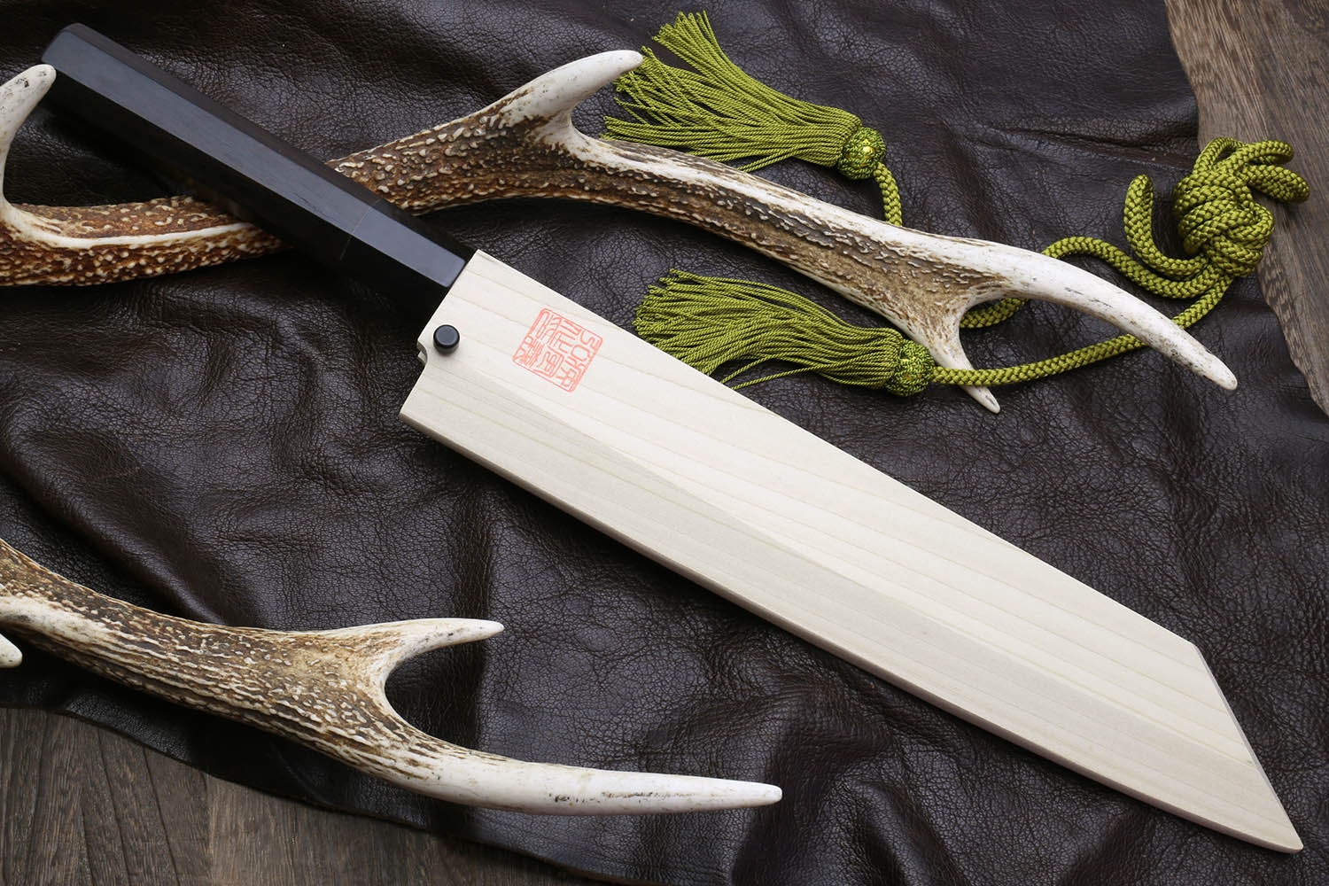 Multipurpose chef knife with silver blade and black handle, light wood sheath and green cord