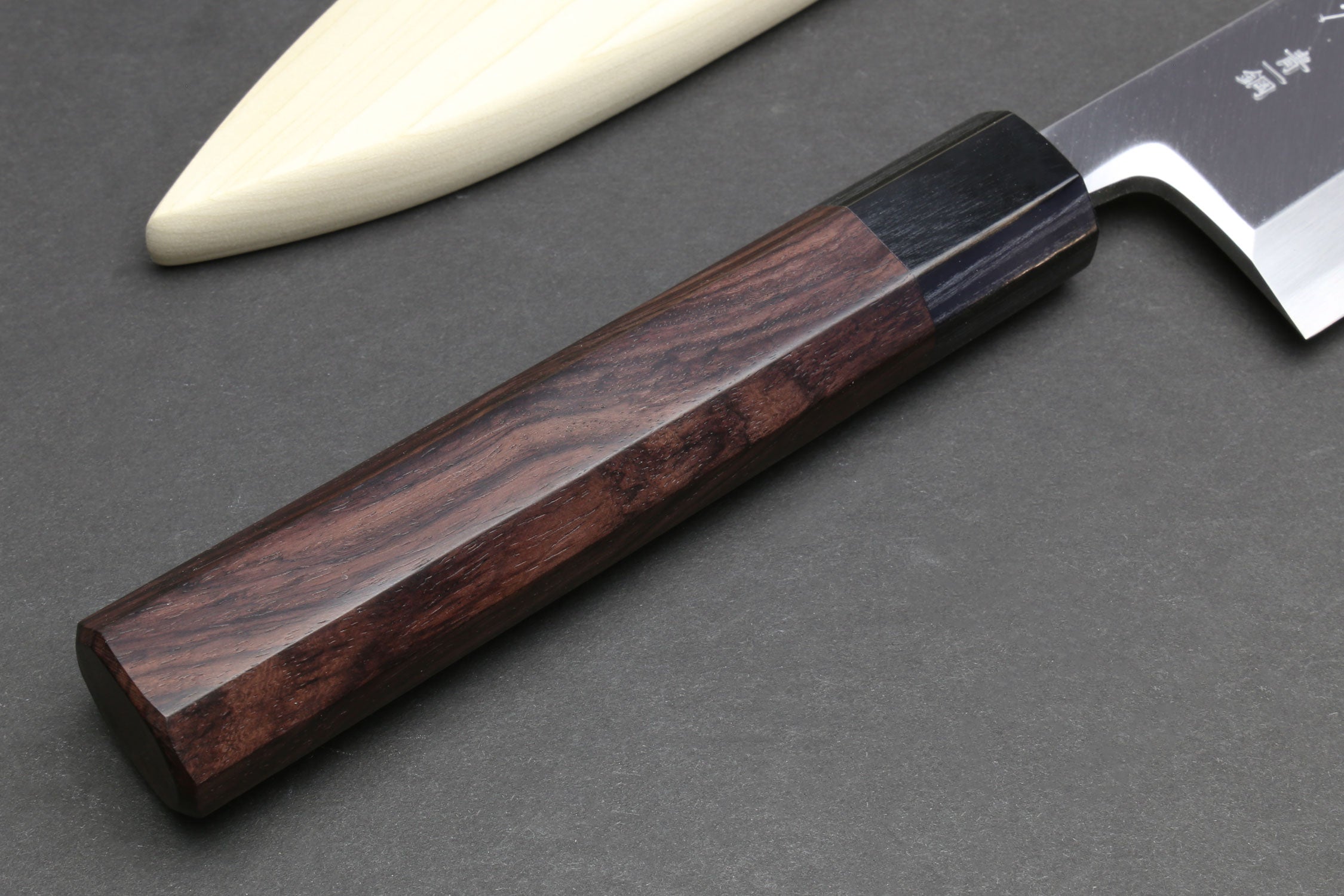 Japanese chef knife handle detail with dark reddish wood and silver bolster