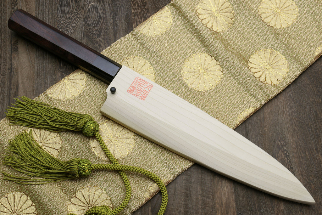 Japanese chef knife with light saya, dark handle, and green tassel cord