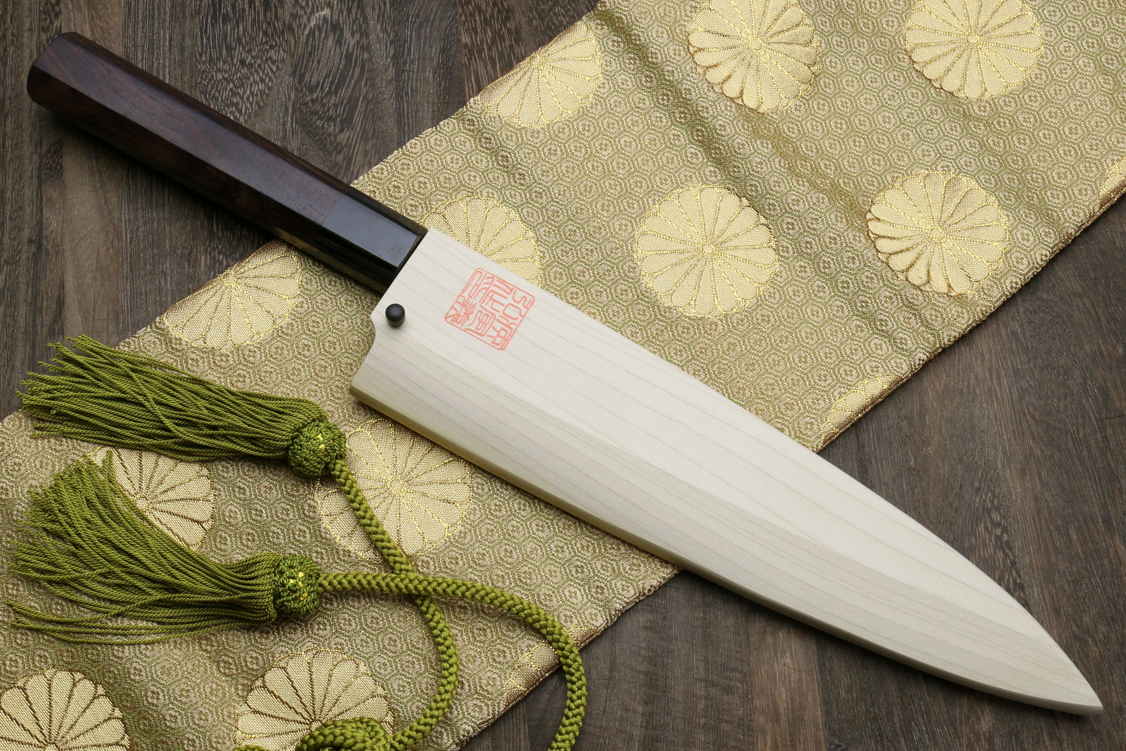 Japanese chef knife with light saya, dark handle, and green tassel cord