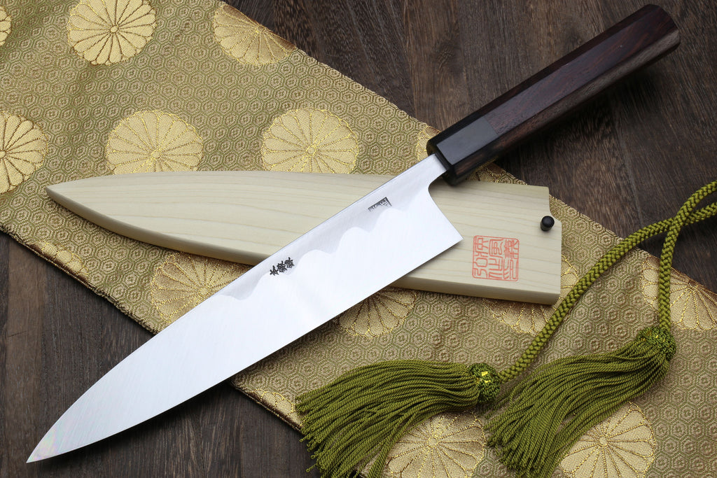 Japanese chef knife with light saya, dark handle, and green tassel cord